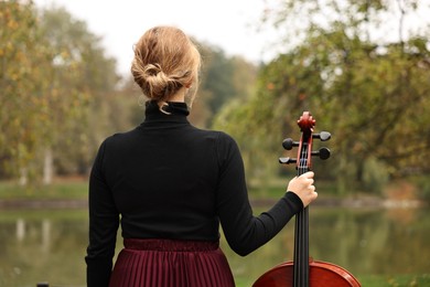 Photo of Woman with cello in park, back view. Classic musical instrument