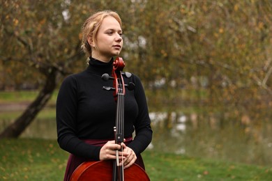 Photo of Beautiful young woman with cello in park, space for text