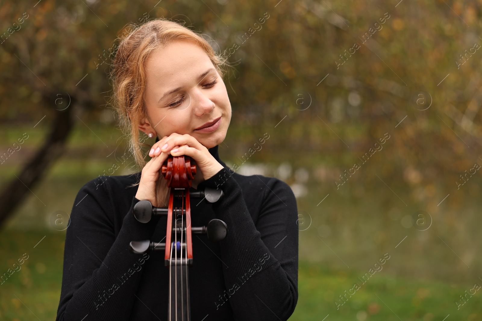 Photo of Beautiful young woman with cello in park, space for text