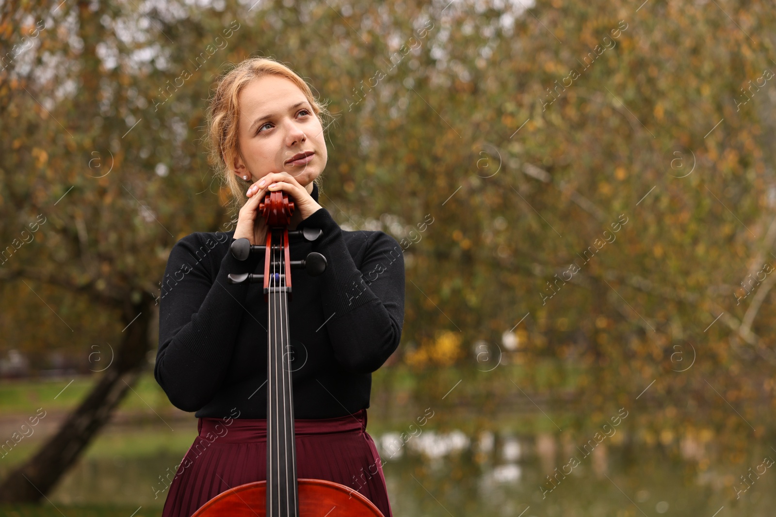 Photo of Beautiful young woman with cello in park, space for text