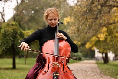 Photo of Beautiful young woman playing cello in park, space for text