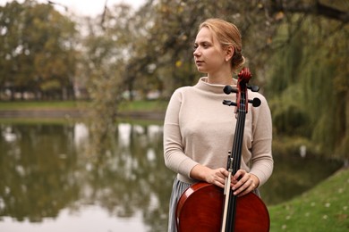 Photo of Beautiful young woman with cello in park, space for text