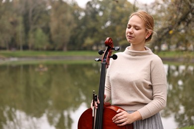 Photo of Beautiful young woman with cello in park, space for text