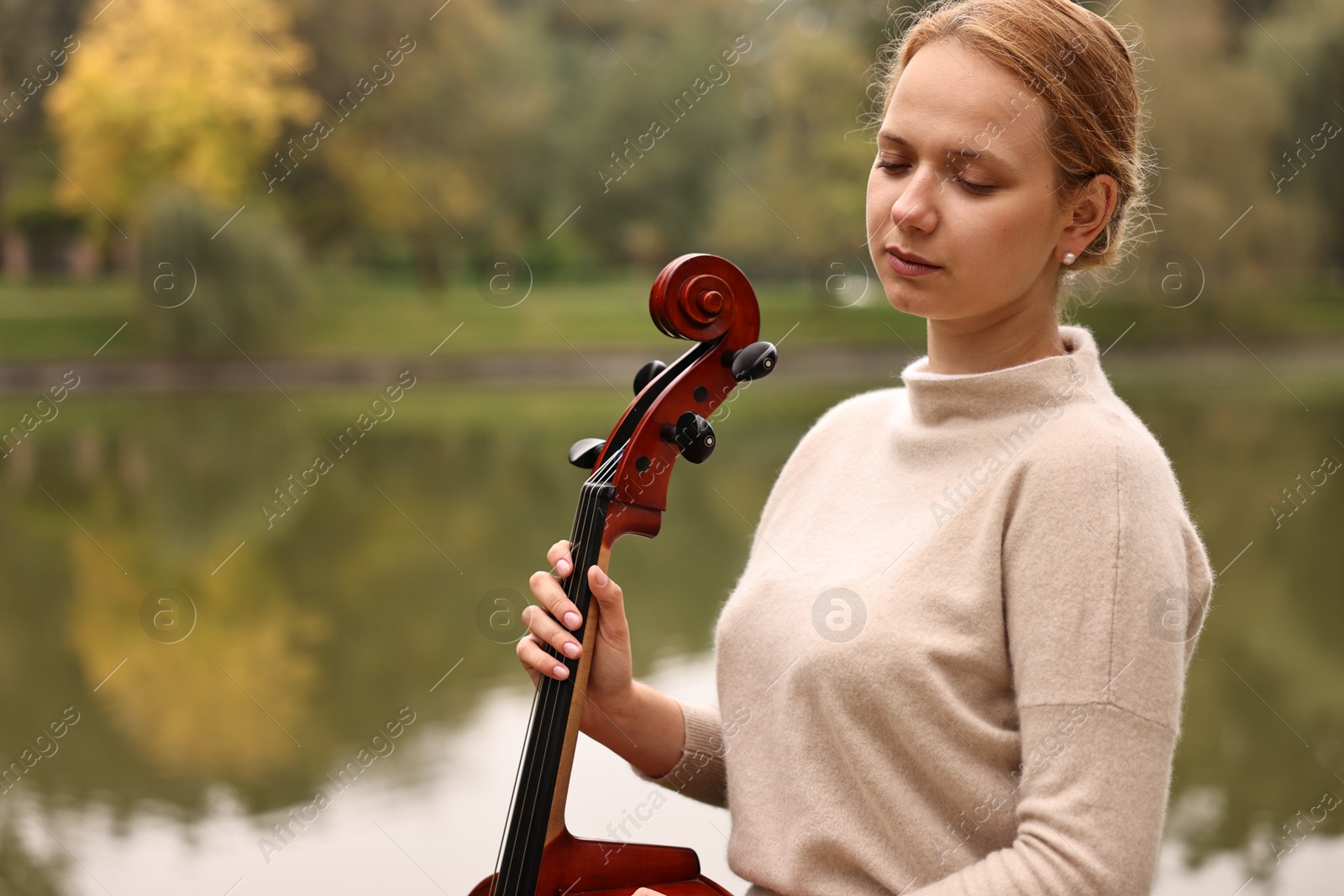 Photo of Beautiful young woman with cello in park, space for text