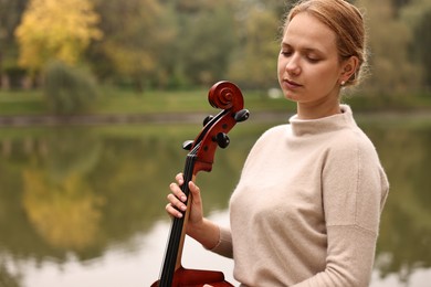 Photo of Beautiful young woman with cello in park, space for text