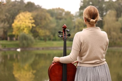 Photo of Young woman with cello in park, back view. Space for text