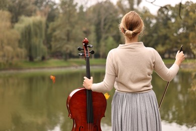 Photo of Woman with cello in park, back view. Classic musical instrument