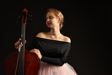 Photo of Beautiful young woman with cello on black background, space for text