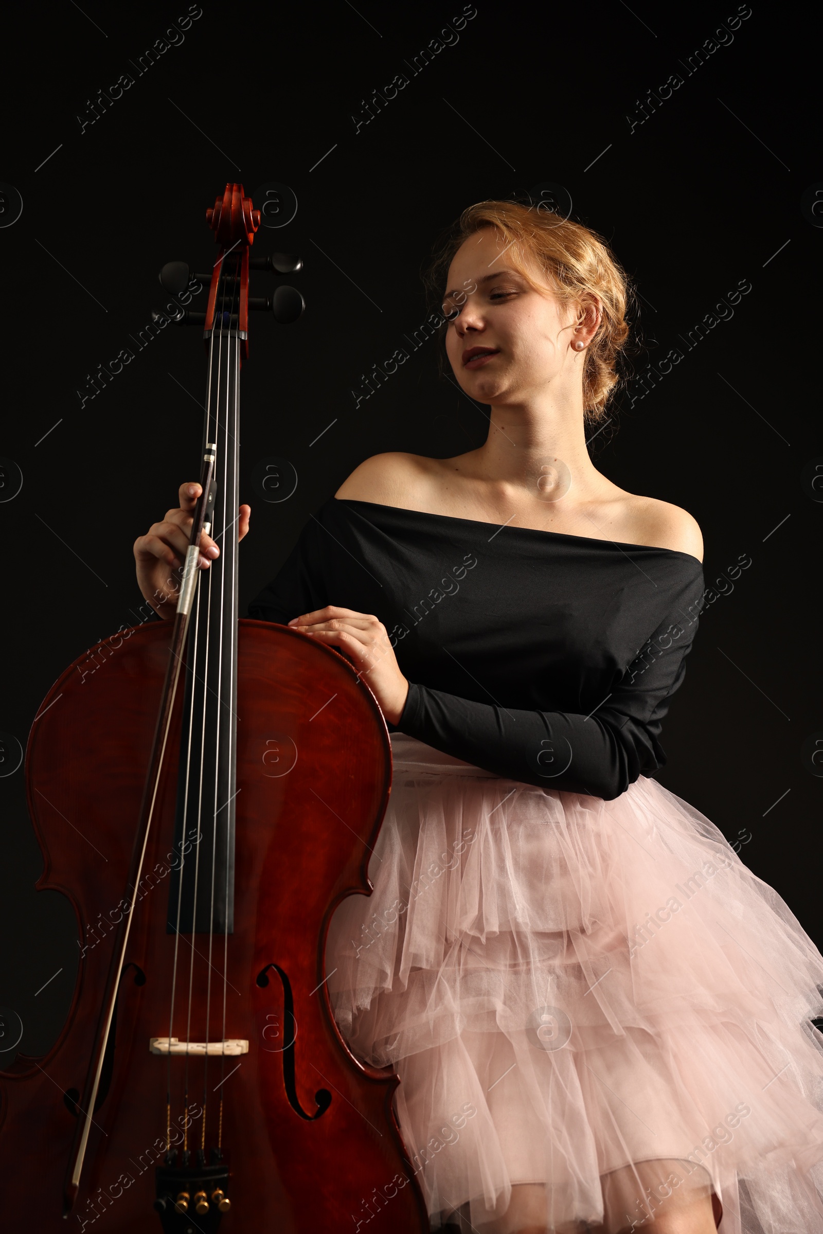 Photo of Beautiful young woman with cello on black background