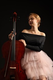 Beautiful young woman with cello on black background