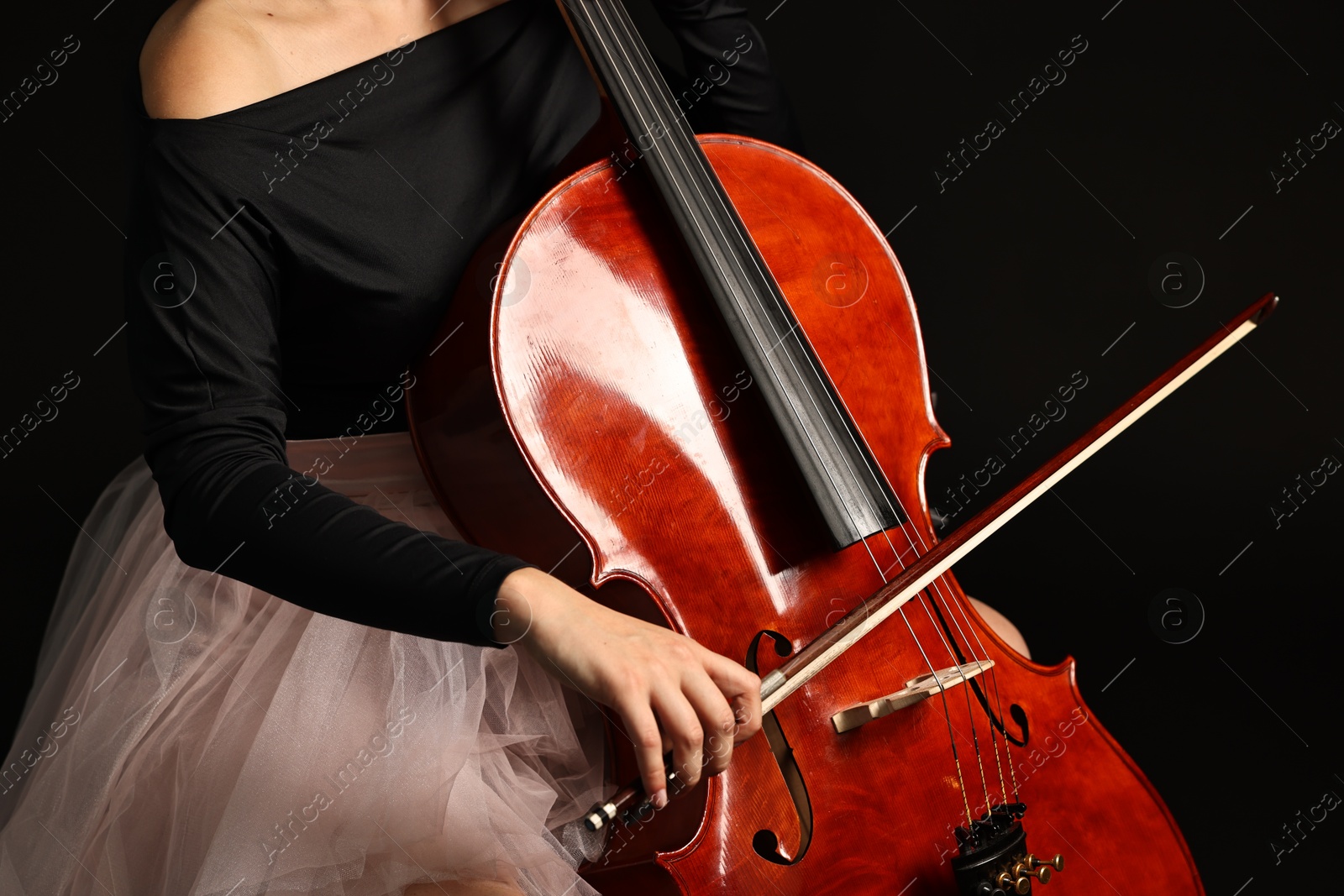 Photo of Young woman playing cello on black background, closeup