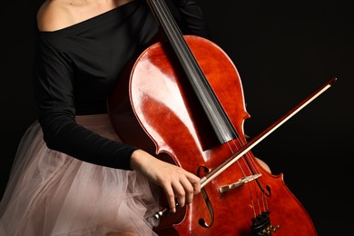 Photo of Young woman playing cello on black background, closeup