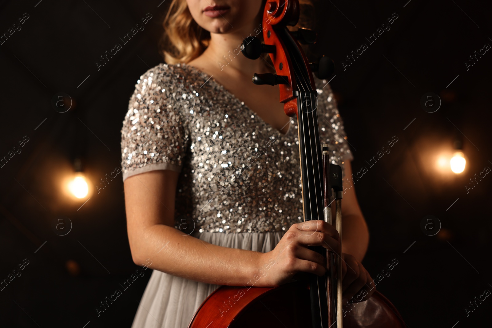 Photo of Young woman with cello on stage, closeup. Classic musical instrument