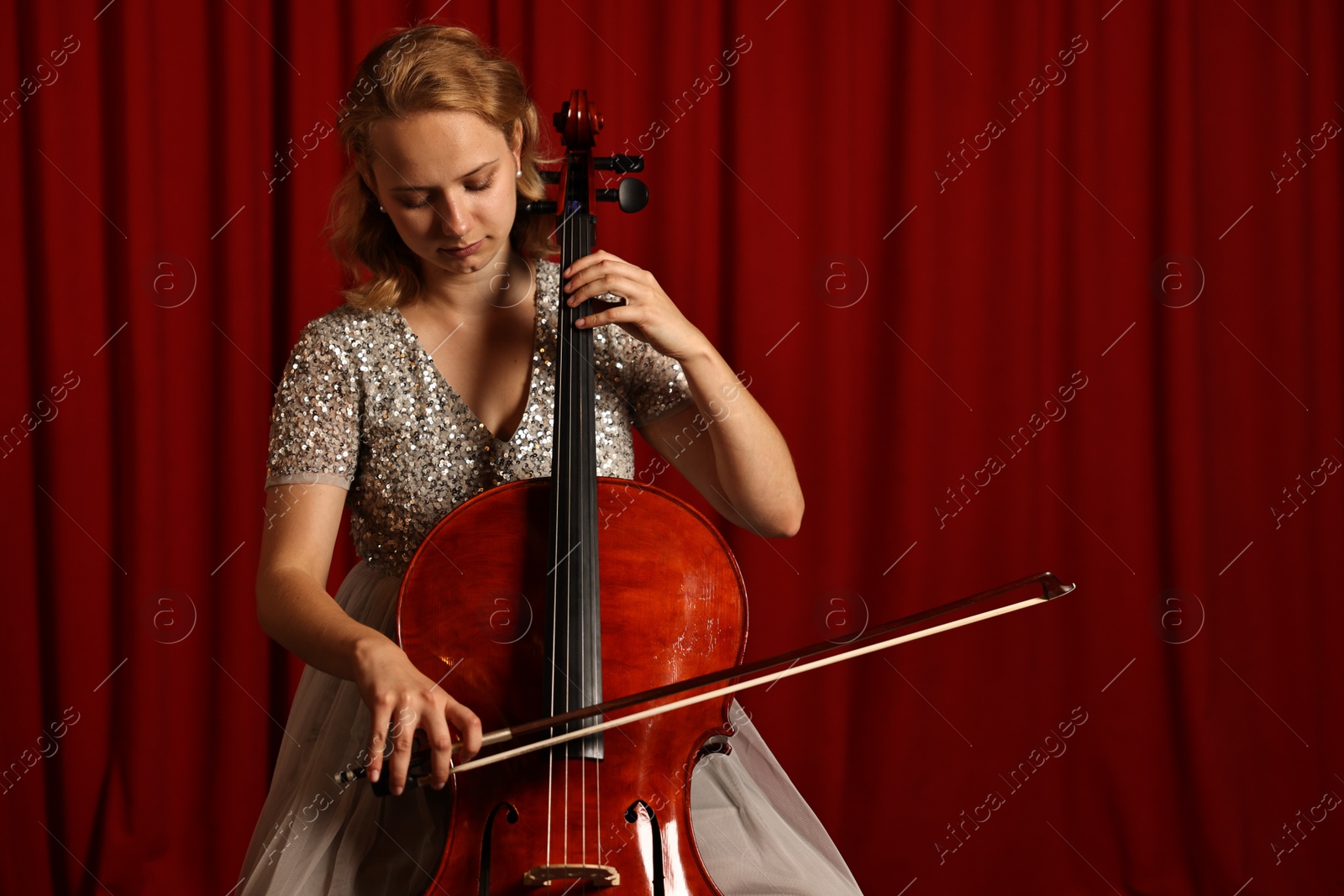 Photo of Beautiful young woman playing cello on stage, space for text