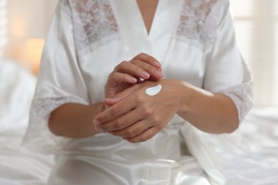 Photo of Woman applying cream onto hand at home, closeup