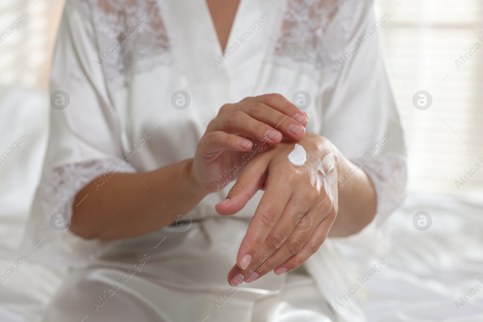 Photo of Woman applying cream onto hand at home, closeup