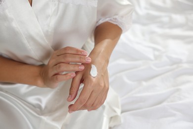 Photo of Woman applying cream onto hand on bed at home, closeup. Space for text