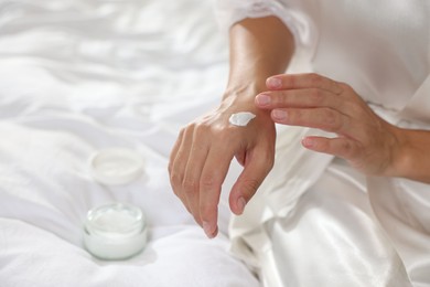 Photo of Woman applying cream onto hand on bed at home, closeup