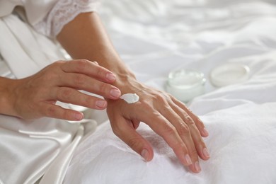 Photo of Woman applying cream onto hand on bed at home, closeup