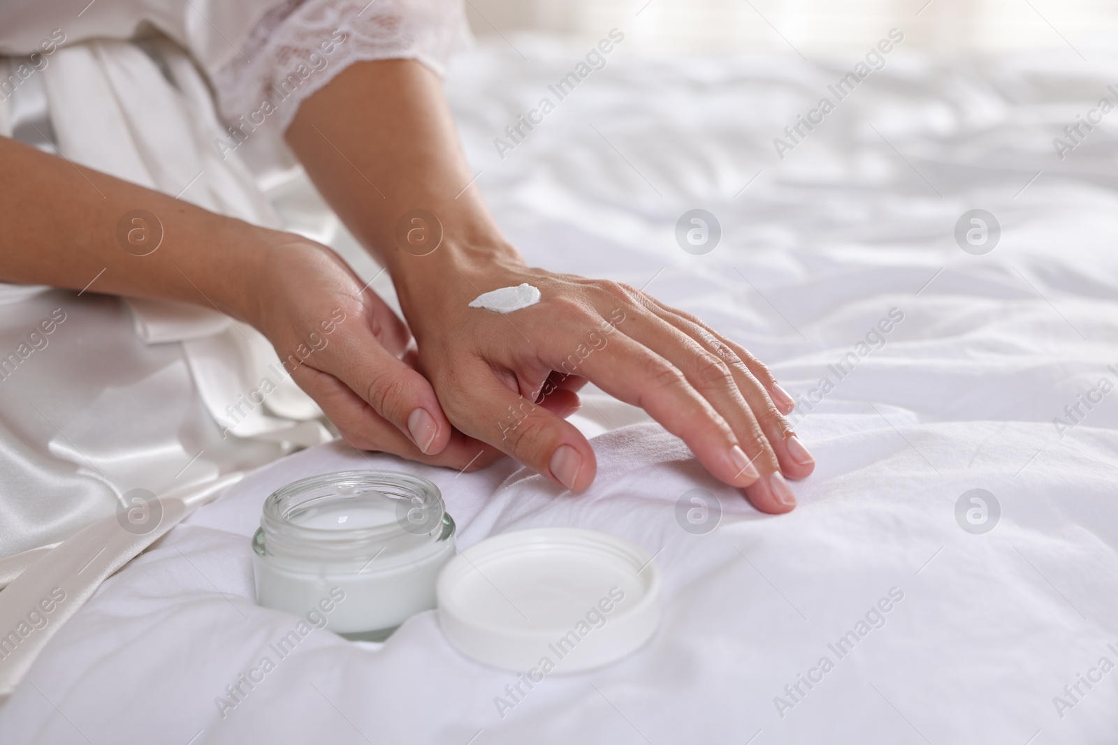 Photo of Woman with jar of cream on bed at home, closeup