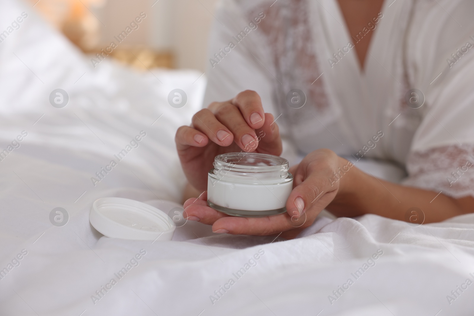 Photo of Woman with jar of cream on bed at home, closeup