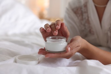 Photo of Woman with jar of cream on bed at home, closeup. Space for text