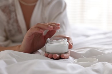 Woman with jar of cream on bed at home, closeup. Space for text