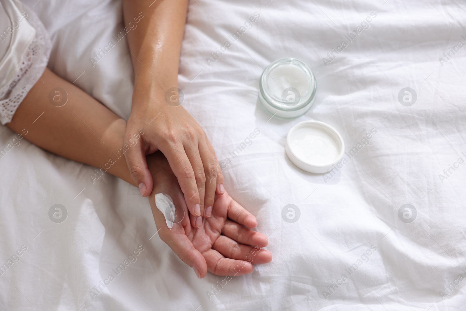 Photo of Woman applying cream onto hand on bed at home, top view