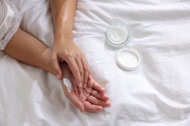 Woman applying cream onto hand on bed at home, top view