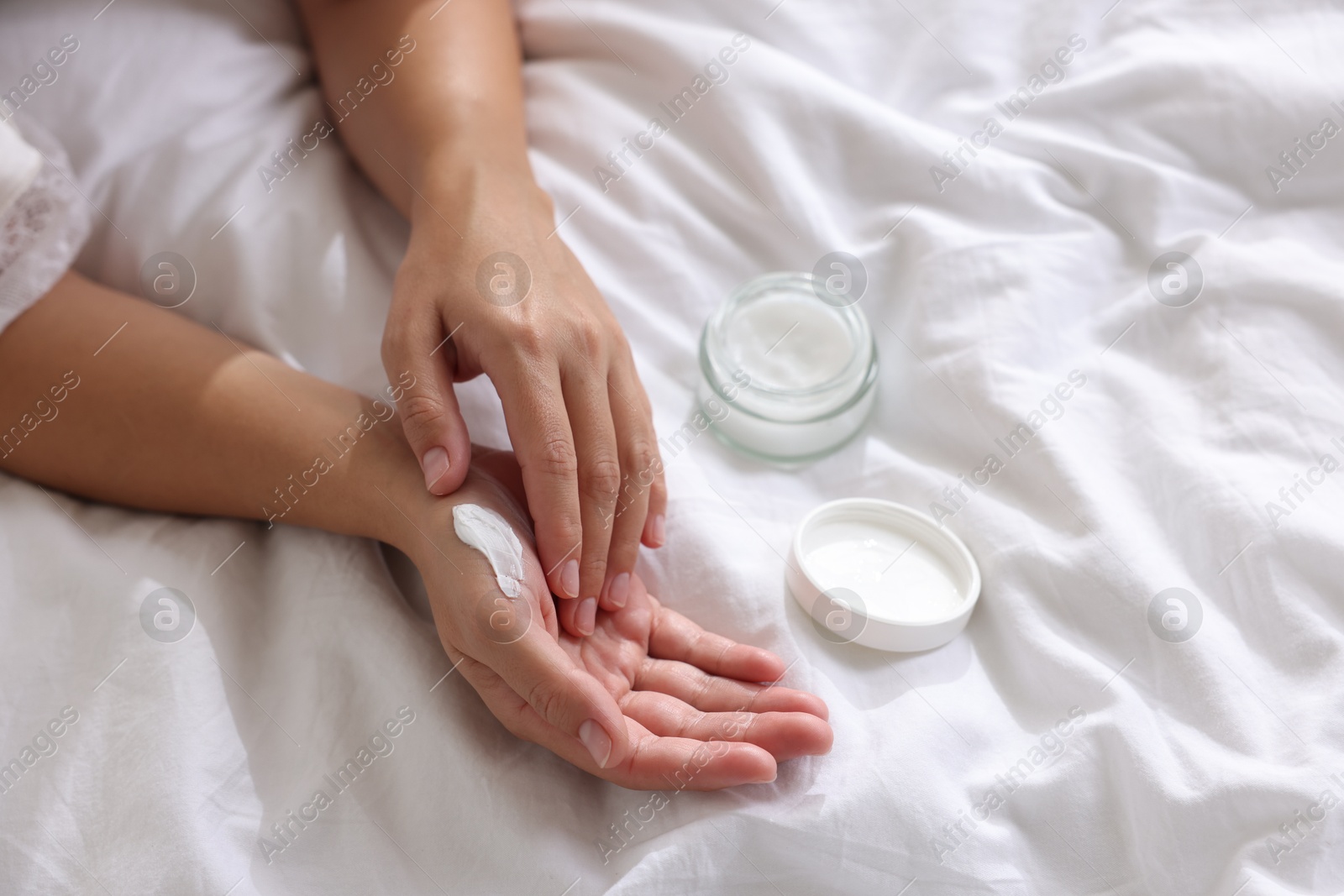 Photo of Woman applying cream onto hand on bed at home, closeup