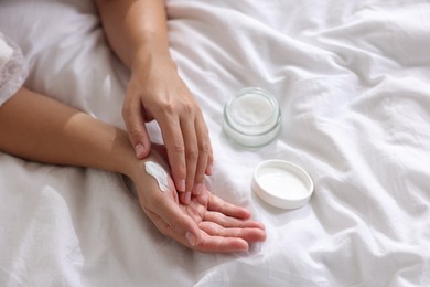 Woman applying cream onto hand on bed at home, closeup