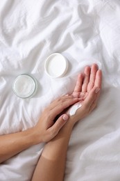 Photo of Woman applying cream onto hand on bed at home, top view