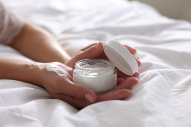 Woman with jar of cream on bed at home, closeup