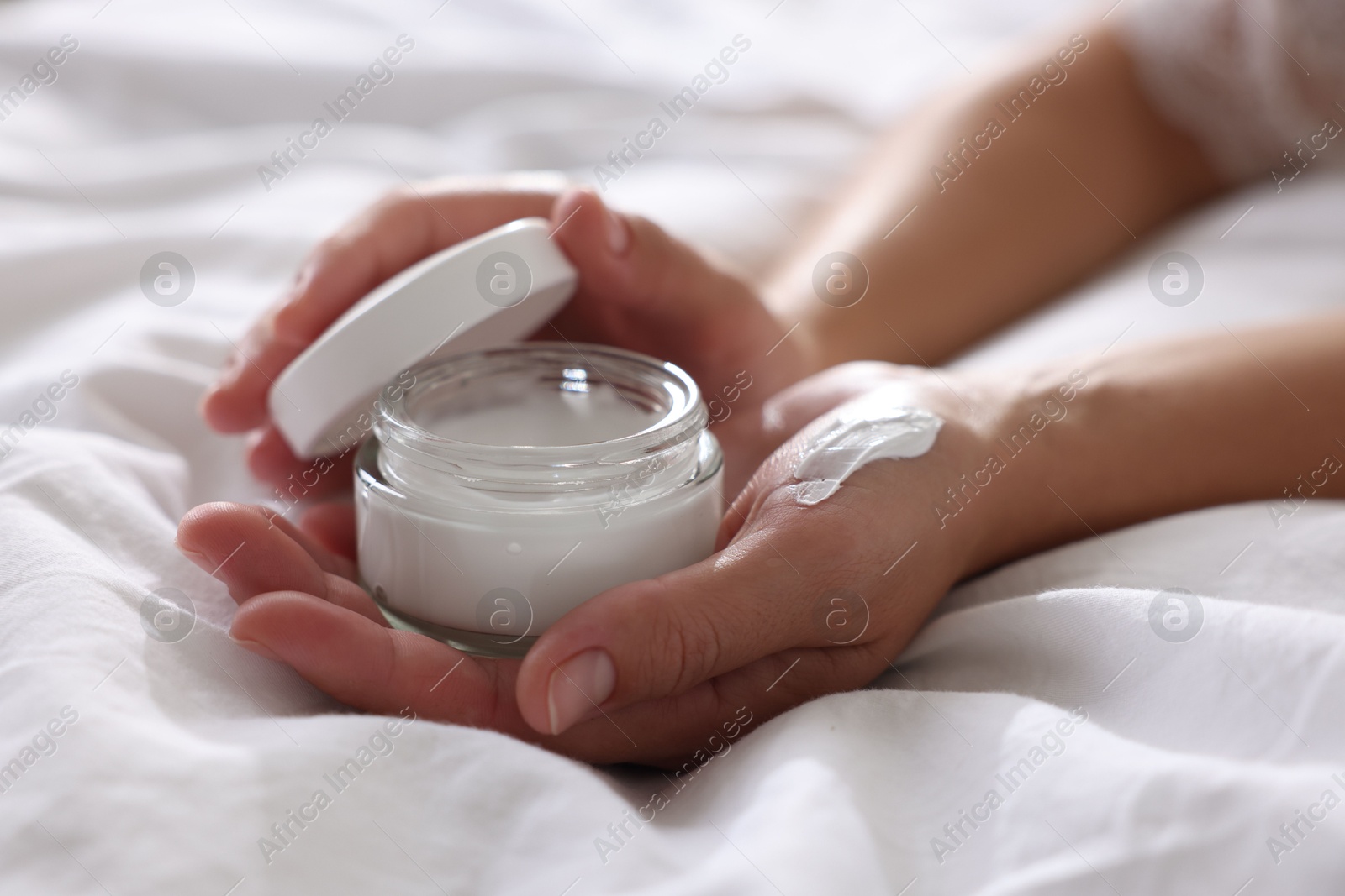 Photo of Woman with jar of cream on bed at home, closeup