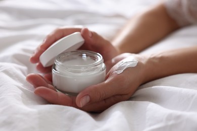 Photo of Woman with jar of cream on bed at home, closeup