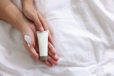 Photo of Woman with tube of cream on bed at home, top view. Space for text