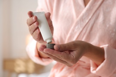 Photo of Woman with tube of cream at home, closeup