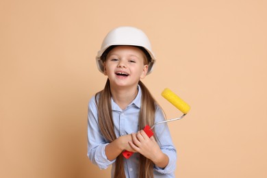 Little girl in hard hat with roller brush on beige background. Dreaming about future profession