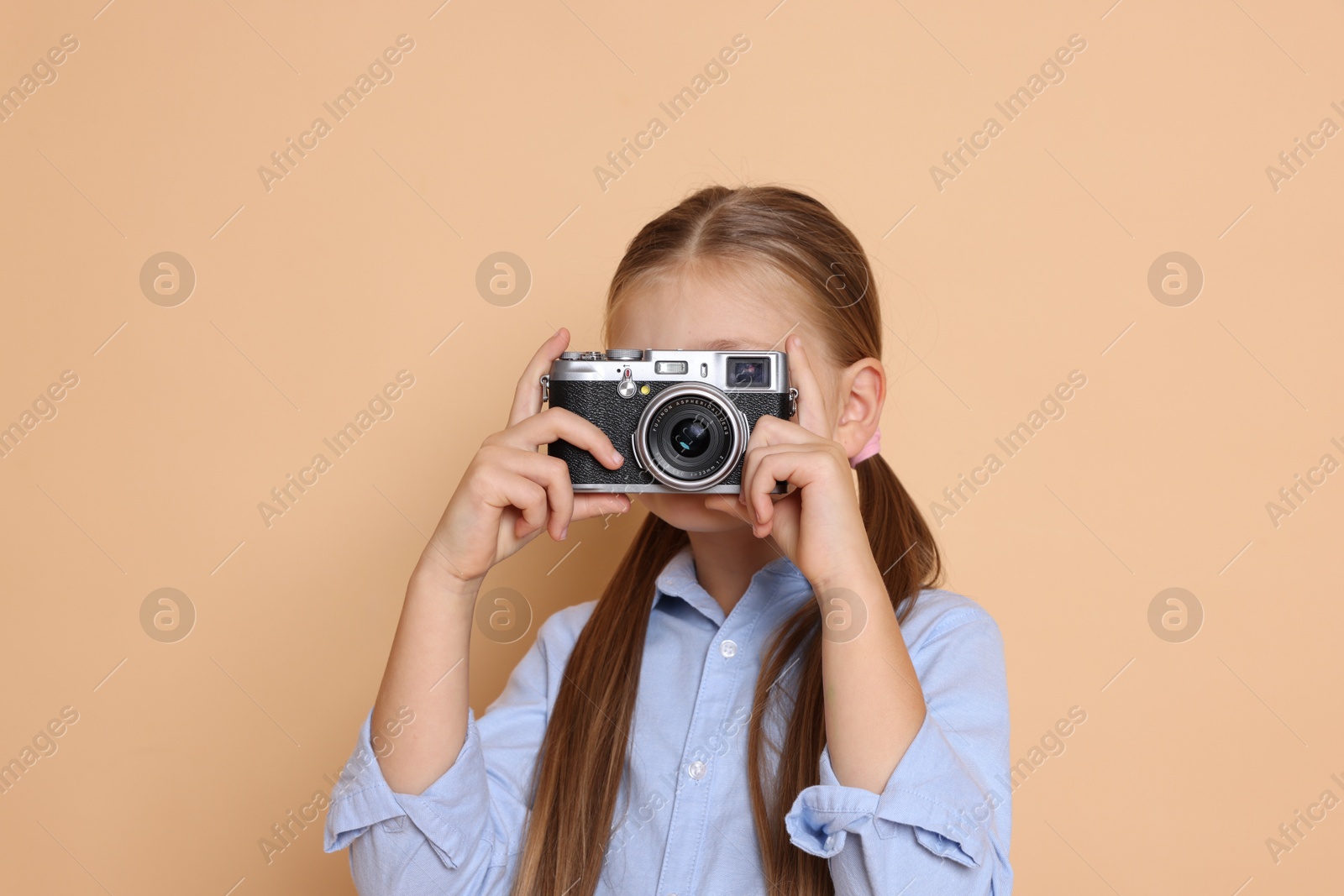 Photo of Little girl with camera pretending to be photographer on beige background. Dreaming of future profession