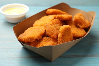 Photo of Delicious chicken nuggets in carton box on blue wooden table, closeup