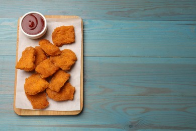 Delicious chicken nuggets with ketchup on blue wooden table, top view. Space for text