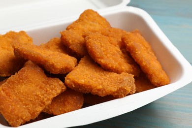 Photo of Delicious chicken nuggets in takeaway container on blue wooden table, closeup