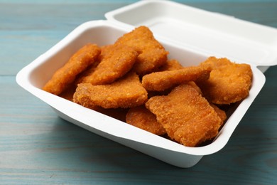 Delicious chicken nuggets in takeaway container on blue wooden table, closeup