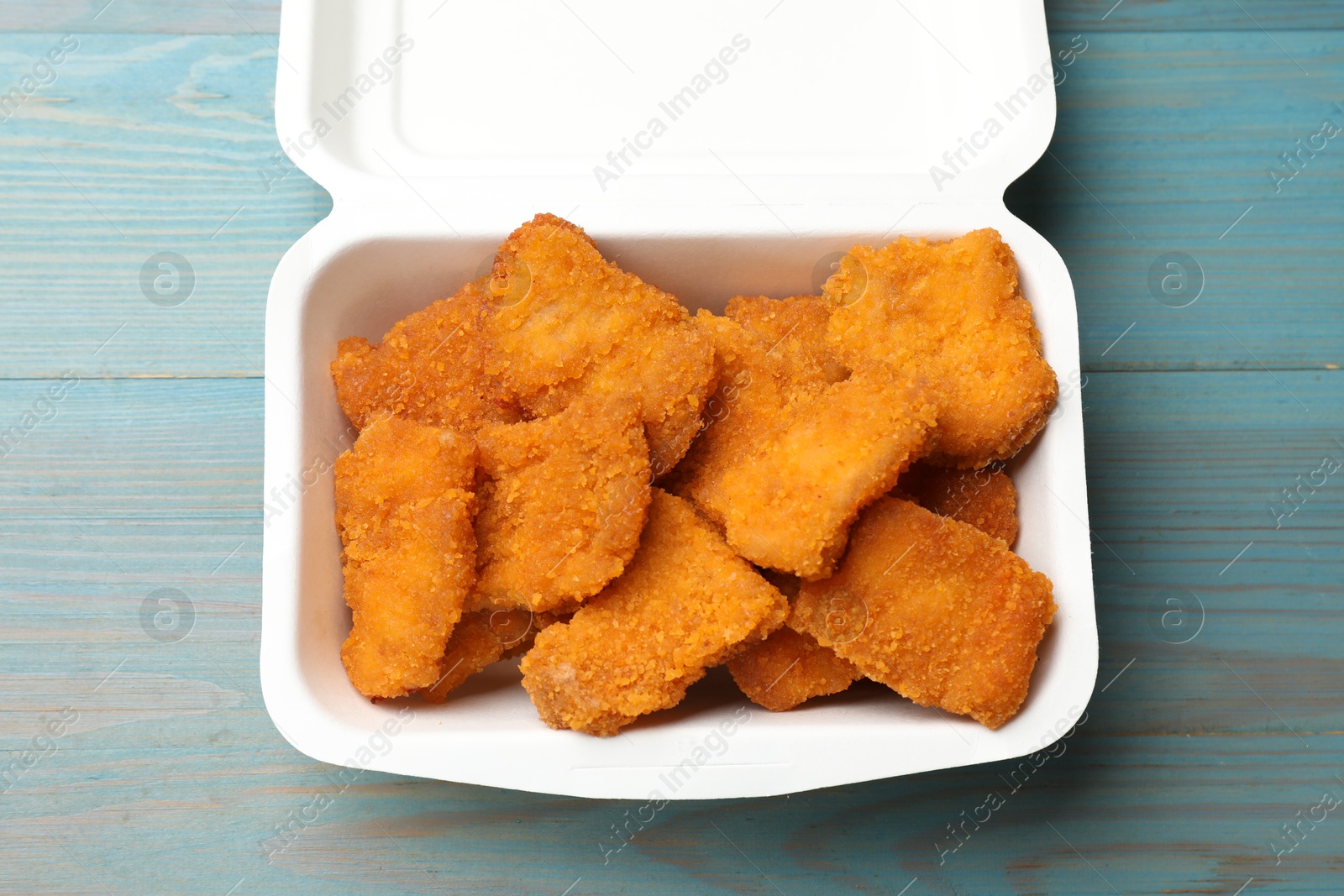 Photo of Delicious chicken nuggets in takeaway container on blue wooden table, top view