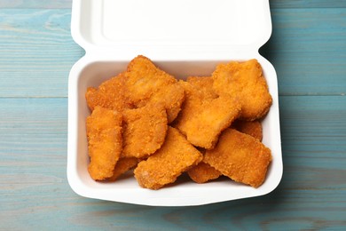 Delicious chicken nuggets in takeaway container on blue wooden table, top view