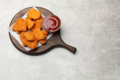 Photo of Delicious chicken nuggets with ketchup on grey textured table, top view. Space for text