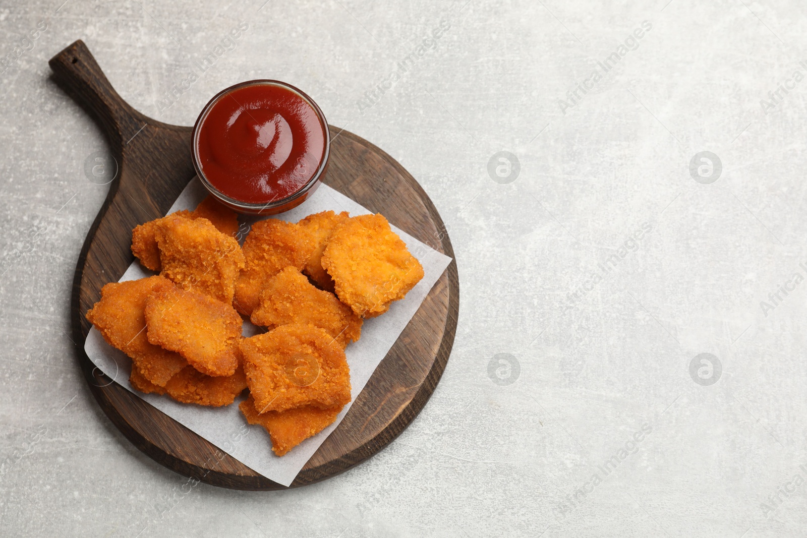 Photo of Delicious chicken nuggets with ketchup on grey textured table, top view. Space for text