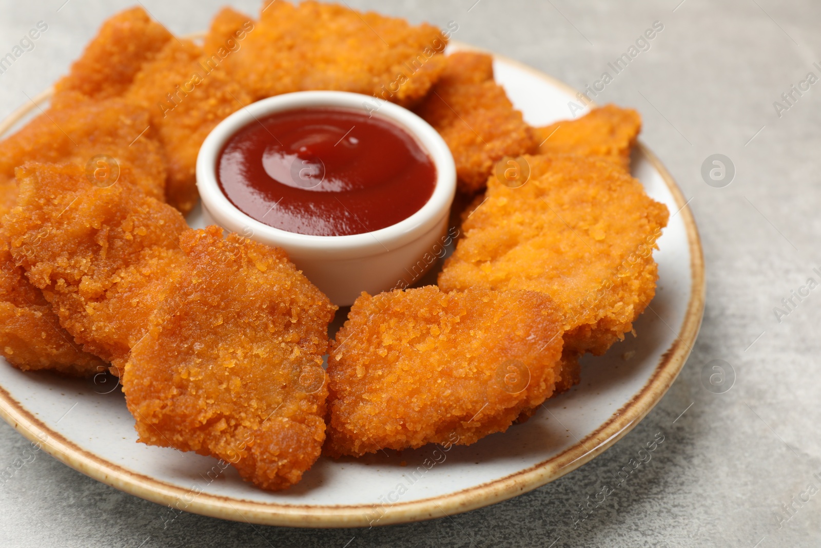 Photo of Delicious chicken nuggets with ketchup on grey textured table, closeup