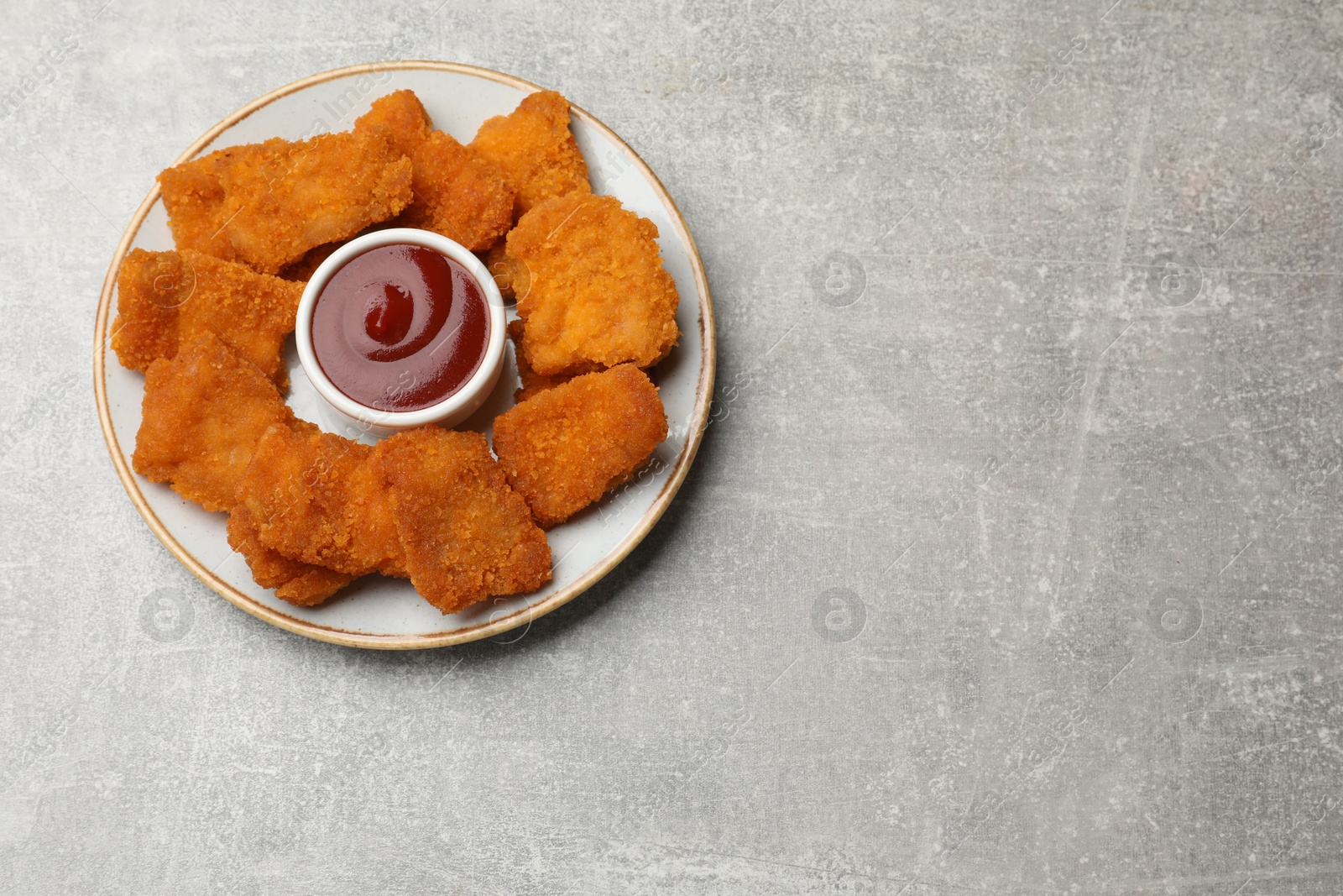 Photo of Delicious chicken nuggets with ketchup on grey textured table, top view. Space for text