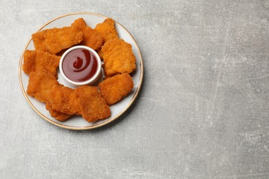 Delicious chicken nuggets with ketchup on grey textured table, top view. Space for text